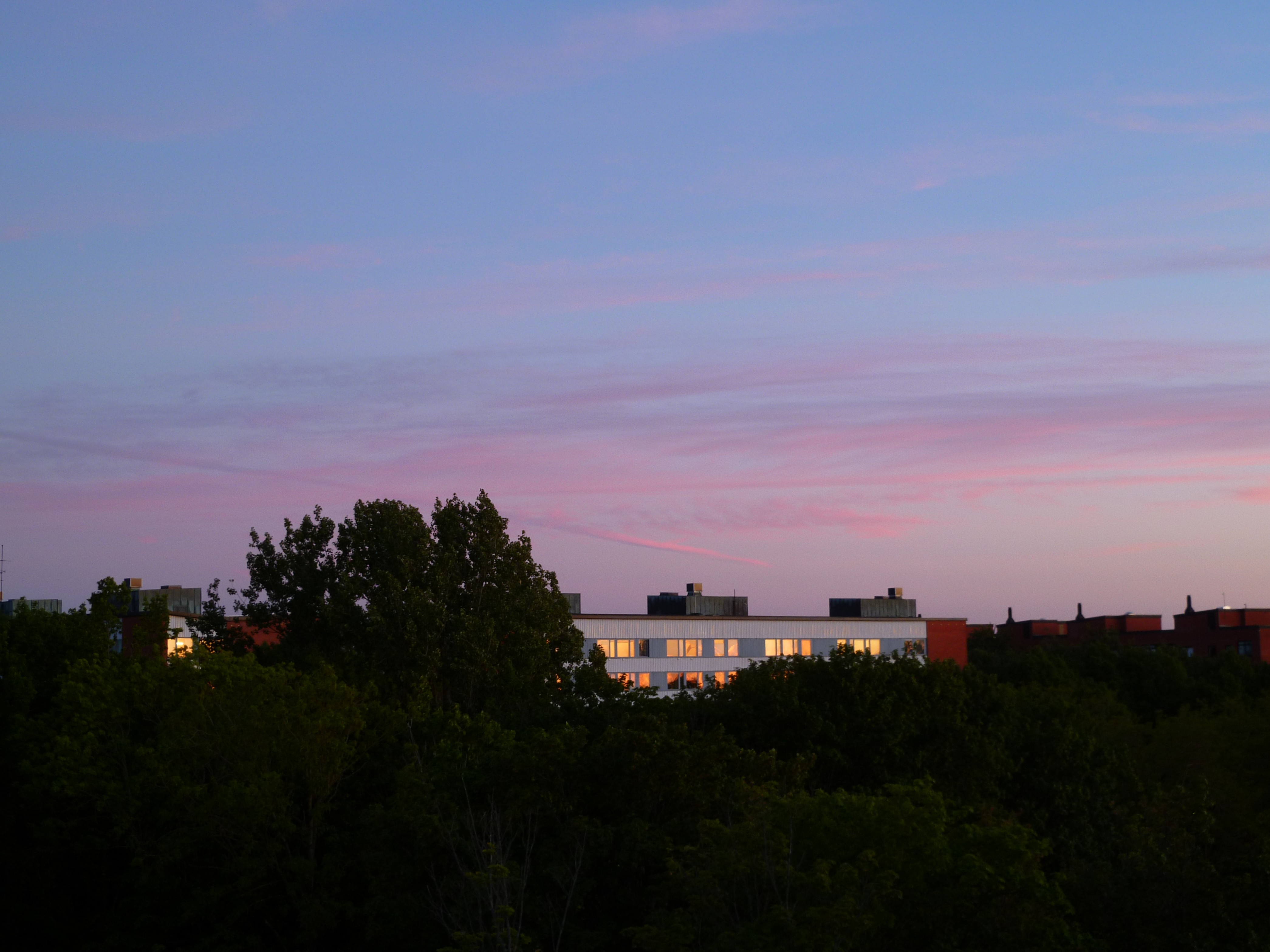 Photo of a pink and blue sunset above an apartment building surrounded by trees